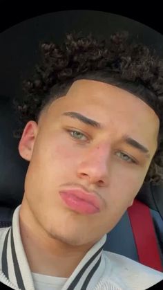 a man with curly hair sitting in the back seat of a car looking at the camera