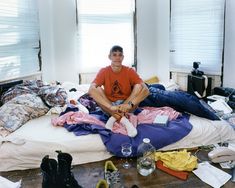 a man sitting on top of a bed surrounded by clutter