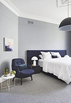 a bedroom with gray walls and white bedding, blue accent chair, black headboard