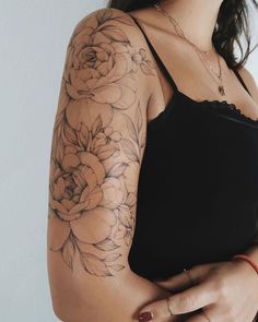 a woman wearing a black tank top with flowers on her arm and shoulder tattoo design