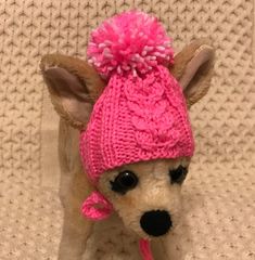 a small dog wearing a pink knitted hat with pom - poms on it's ears