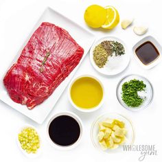 raw meat and ingredients laid out on a white plate, including lemons, garlic, parsley, seasoning, salt, pepper, butter, oil, and other spices