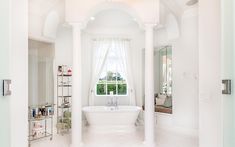 a white bathroom with an arched ceiling and tub in the center, surrounded by columns