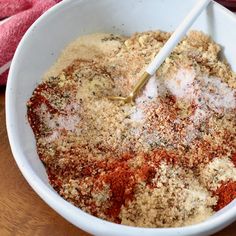 a white bowl filled with spices on top of a wooden table next to a red towel