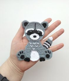 a hand holding a small crocheted raccoon