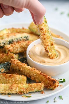 someone dipping something in a small white bowl on top of some fried zucchini