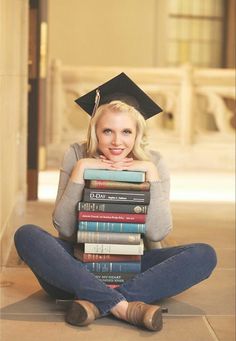 a woman sitting on the floor with her legs crossed and holding a stack of books