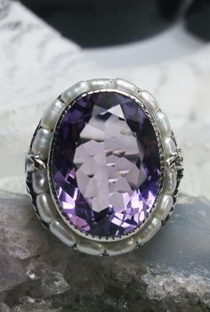 Natural Purple Amethyst & Pearl Ring Leaf Pearl Design#156 This is a stunning 9.5 carat natural purple amethyst gemstone ring. The natural amethyst gem has amazing color and clarity. This gemstone is 12mm x 16mm in dimensions (10/16" x 9/16"). The garden themed filigree circles the edge of the ring and extends down the band accenting the beautiful large gemstone. Seed pearls frame the large gemstone, creating a vibrant contrast. Holding the seed pearls in place are 2 silver leaves and fine w Exquisite Amethyst Ring, Exquisite Amethyst Ring For Anniversary, Elegant Large Stone Amethyst Ring, Exquisite Purple Amethyst Ring For Anniversary, Exquisite Amethyst Ring With Gemstone Accents, Exquisite Silver Amethyst Ring, Exquisite Amethyst Gemstone Rings, Exquisite Purple Amethyst Ring With Gemstone Accents, Classic Amethyst Ring As A Gift