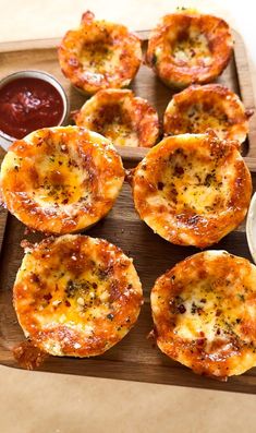 several mini pizzas on a wooden tray with ketchup