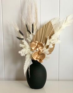 a black vase with white and gold flowers in it