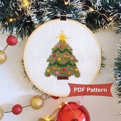 a cross stitch christmas tree ornament hanging on a wall next to some ornaments