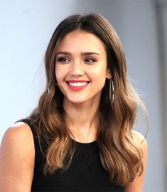 a woman with long hair smiles at the camera while wearing a black dress and large hoop earrings