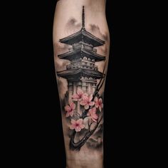 a black and white tattoo with pink flowers on the leg, in front of a pagoda