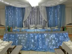 a banquet table set up with white plates and silverware on it, in front of blue drapes