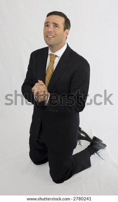 a man in a suit and tie sitting on the ground with his hands folded up