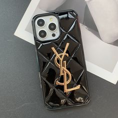 a black phone case with a gold y on it sitting next to a white vase