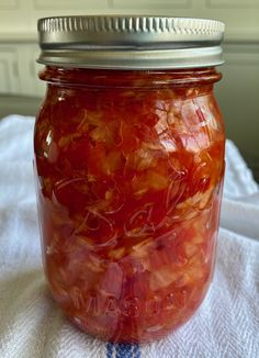 a jar filled with lots of red food on top of a white table cloth next to a window