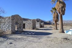 an old stone building with palm trees in the foreground and mountains in the background