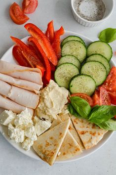 a white plate topped with lots of different types of food next to cucumbers and tomatoes