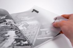 a person holding an open book with black and white photos on it, in front of a cityscape