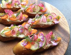 several pieces of bread with various vegetables on them sitting on a wooden platter, ready to be eaten