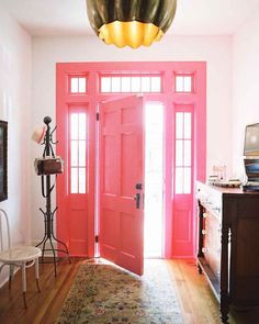 a bright pink door in a white room with an antique rug on the hardwood floor