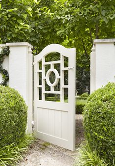 an open white gate in the middle of some bushes