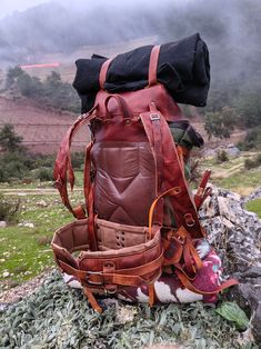 a large brown backpack sitting on top of a pile of rocks next to a field