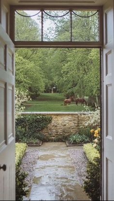 an open door leading to a lush green yard with horses grazing in the pasture behind it