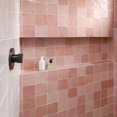 a bathroom with pink tiles on the wall and soap dispenser next to it