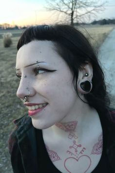 a woman with piercings on her face and nose is standing in front of a dirt road