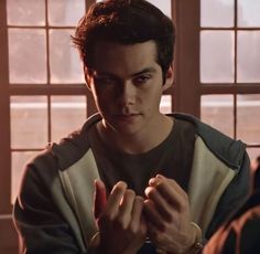 a young man sitting at a table in front of a window holding his hands together