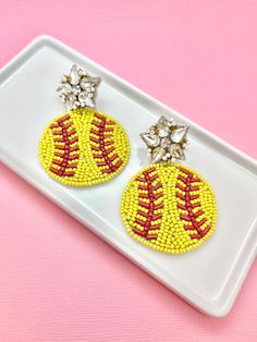 two beaded baseball earrings on a white tray against a pink background with silver stars