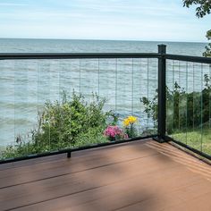 a deck overlooking the ocean with flowers and trees in the foreground, on which there is a bench