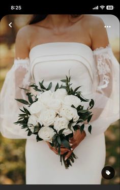 a woman in a white wedding dress holding a bridal bouquet with greenery on it