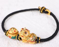 A 24k Real Gold Bracelet with a traditional Chinese lion-dance and treasure bowl is carefully handmade to commemorate wealth, fortune, strength, and good luck. The Lion-Dance charm is made of 24K 999 Pure Gold and is 14mm wide, 16mm long, and 10.5mm high. Meanwhile, the Treasure Bowl charm has a diameter of 11.3 mm and a height of 11.1 mm, making a total gold weight of approximately 3.1 g. This minimalist style bracelet features a handmade hand braided bracelet cord that is adjustable to fit com Gold Spiritual Braided Bracelet For Good Luck, Gold Braided Bracelet For Good Luck, Traditional Wristband Bracelet For Gifts, Traditional Adjustable Braided Bracelets For Festivals, Handmade Adjustable Traditional Gold Bracelet, Handmade Traditional Gold Bracelet, Traditional Adjustable Gold Beaded Bracelets, Traditional Handmade Adjustable Gold Bracelet, Traditional Gold Beaded Adjustable Bracelet