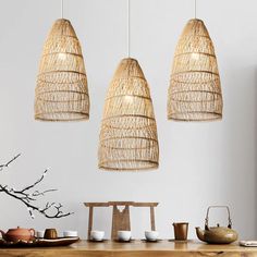 three lights hanging from the ceiling over a wooden table with tea cups and bowls on it