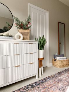 a white dresser sitting next to a mirror on top of a wooden cabinet in a room