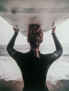 a woman holding a surfboard over her head while standing in front of the ocean