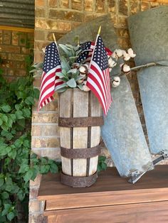 an old barrel with american flags on it is sitting next to a planter filled with flowers