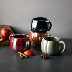 three mugs sitting on top of a table next to an apple and cinnamon stick