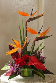 an arrangement of flowers and birds of paradise in a vase on top of a table