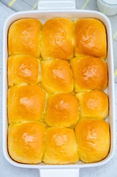 a white casserole dish filled with yellow bread rolls and sitting on a table