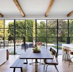 a dining room table with chairs and a bowl of fruit on it in front of large windows