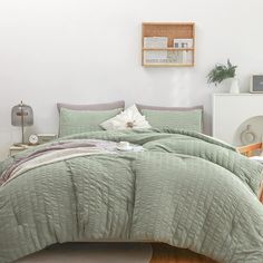 a bed with green comforter and pillows in a room next to a white wall