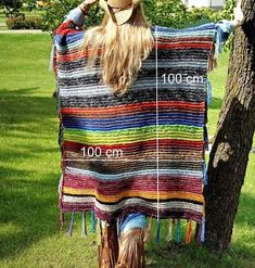 a woman wearing a cowboy hat standing next to a tree with a colorful blanket on it