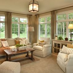 a living room filled with lots of furniture next to two large windows covered in curtains