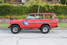 a red suv parked on the side of a road next to a green hedge covered wall