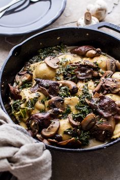 a skillet filled with mushrooms and cheese on top of a table next to utensils