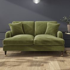 a green couch sitting on top of a wooden floor next to a vase filled with flowers